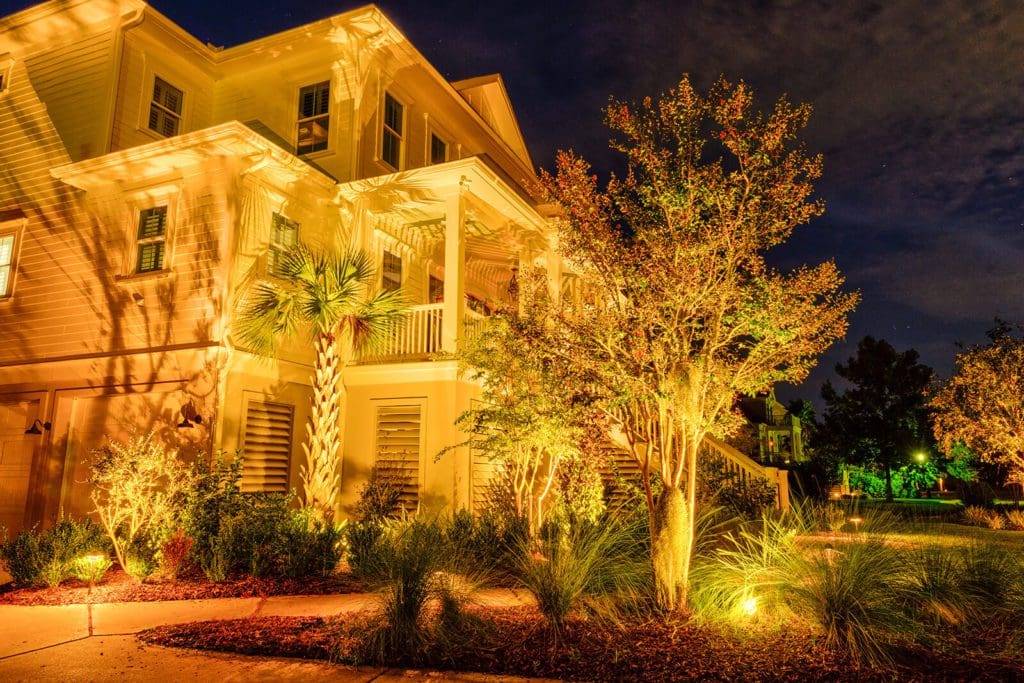 Nighttime landscape lighting on a coastal home with uplighting on palms and live oaks and path lighting, by MP Landscape Design