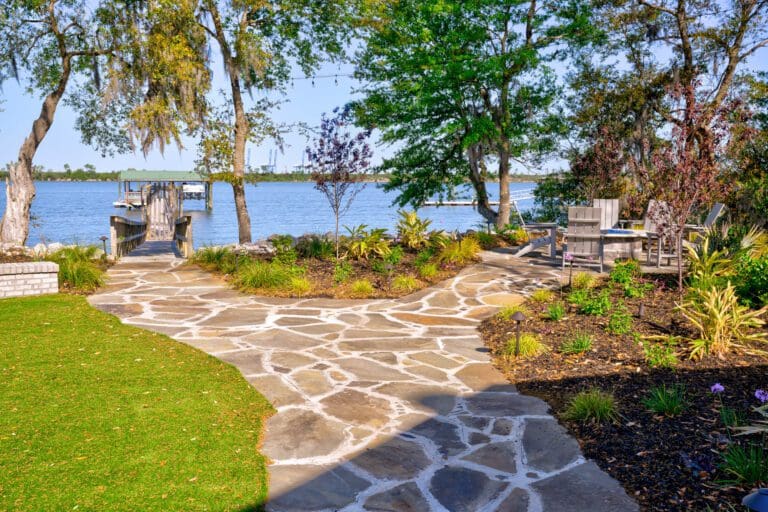 Fully redesigned Lowcountry backyard with a flagstone patio, layered planting beds, live oaks draped in Spanish moss, and a dock on the water