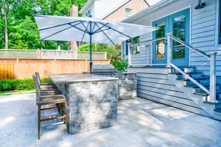 Outdoor kitchen with a stone-clad grill island and bar seating on a paver patio beside a Mount Pleasant, SC home
