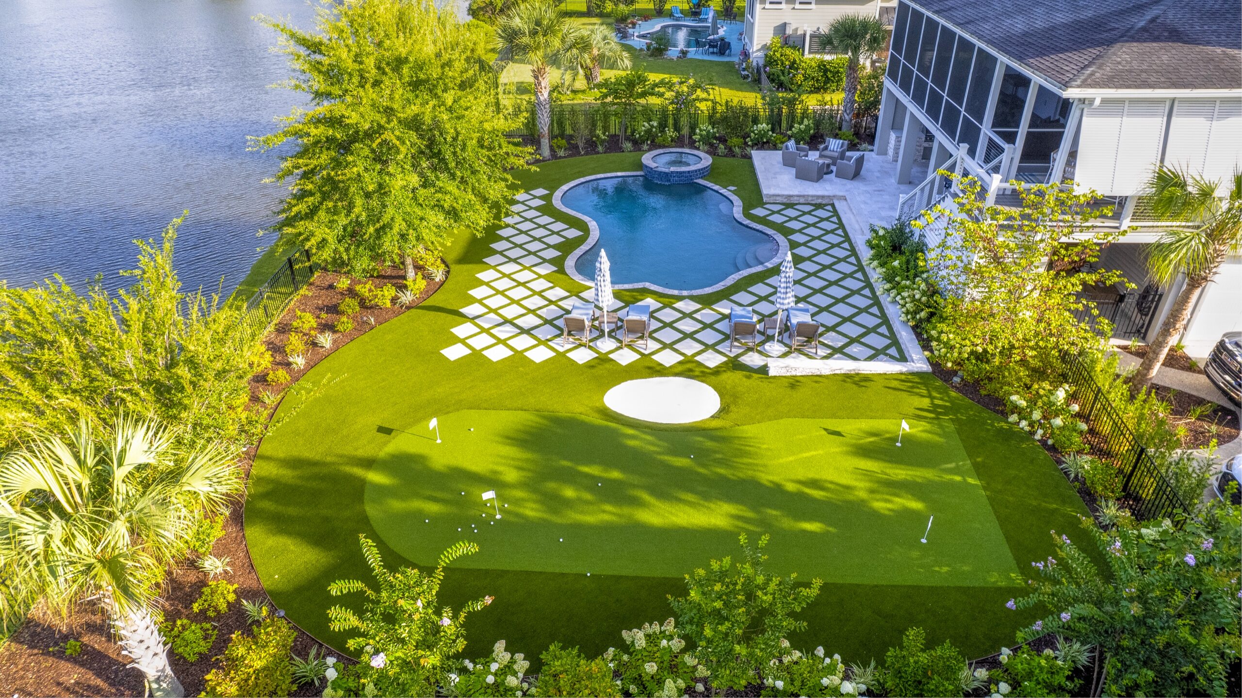 Aerial of the waterfront backyard with putting green, pool and paver patio at golden hour